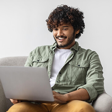 Young man sitting on a chair and smiling while using a laptop