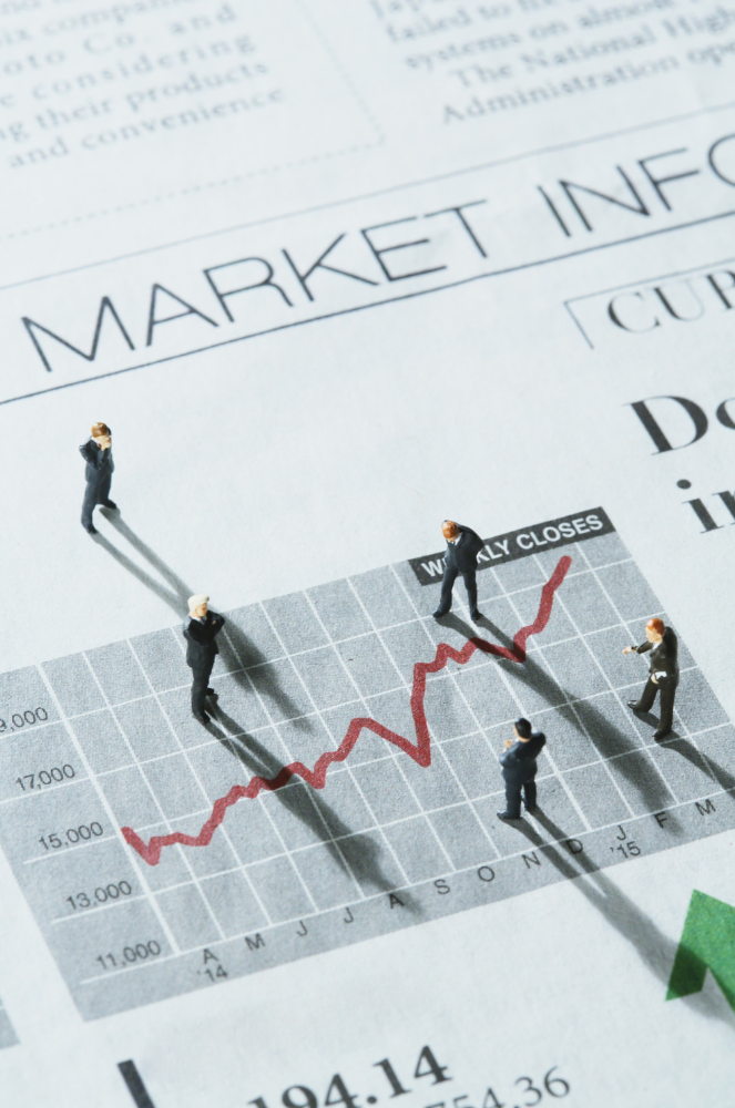 Small figurines standing on a printed stock market chart showing rising and falling trends