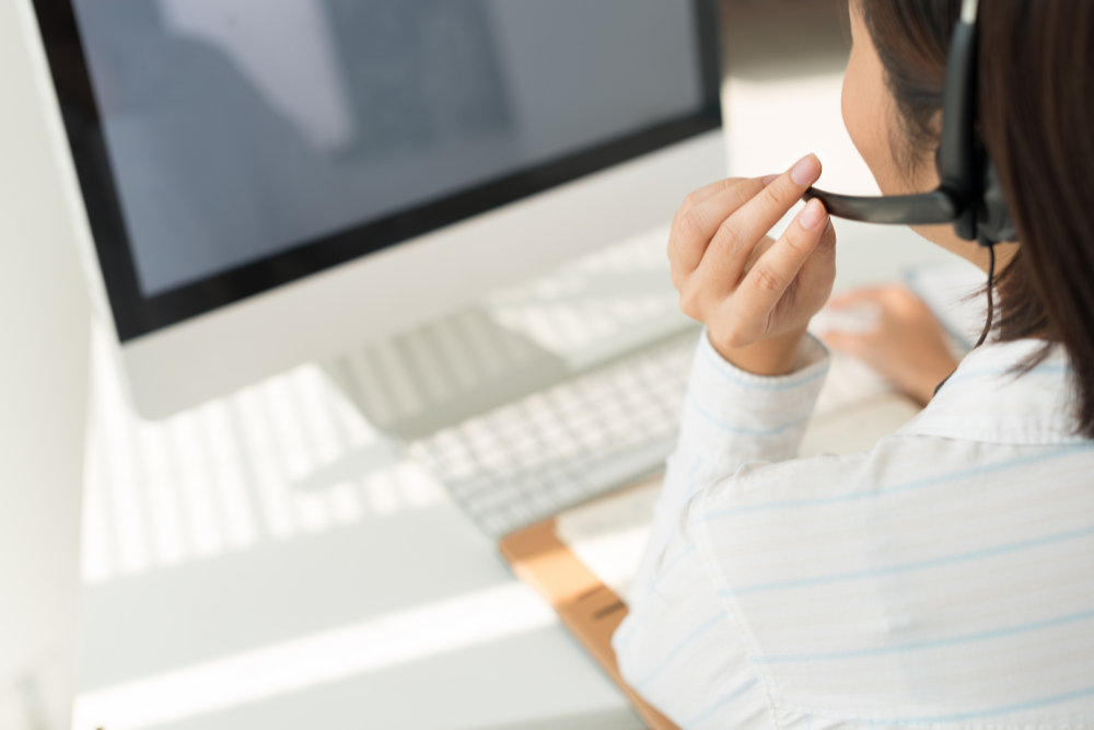 Woman using a headset while working at a desktop computer in a bright office
